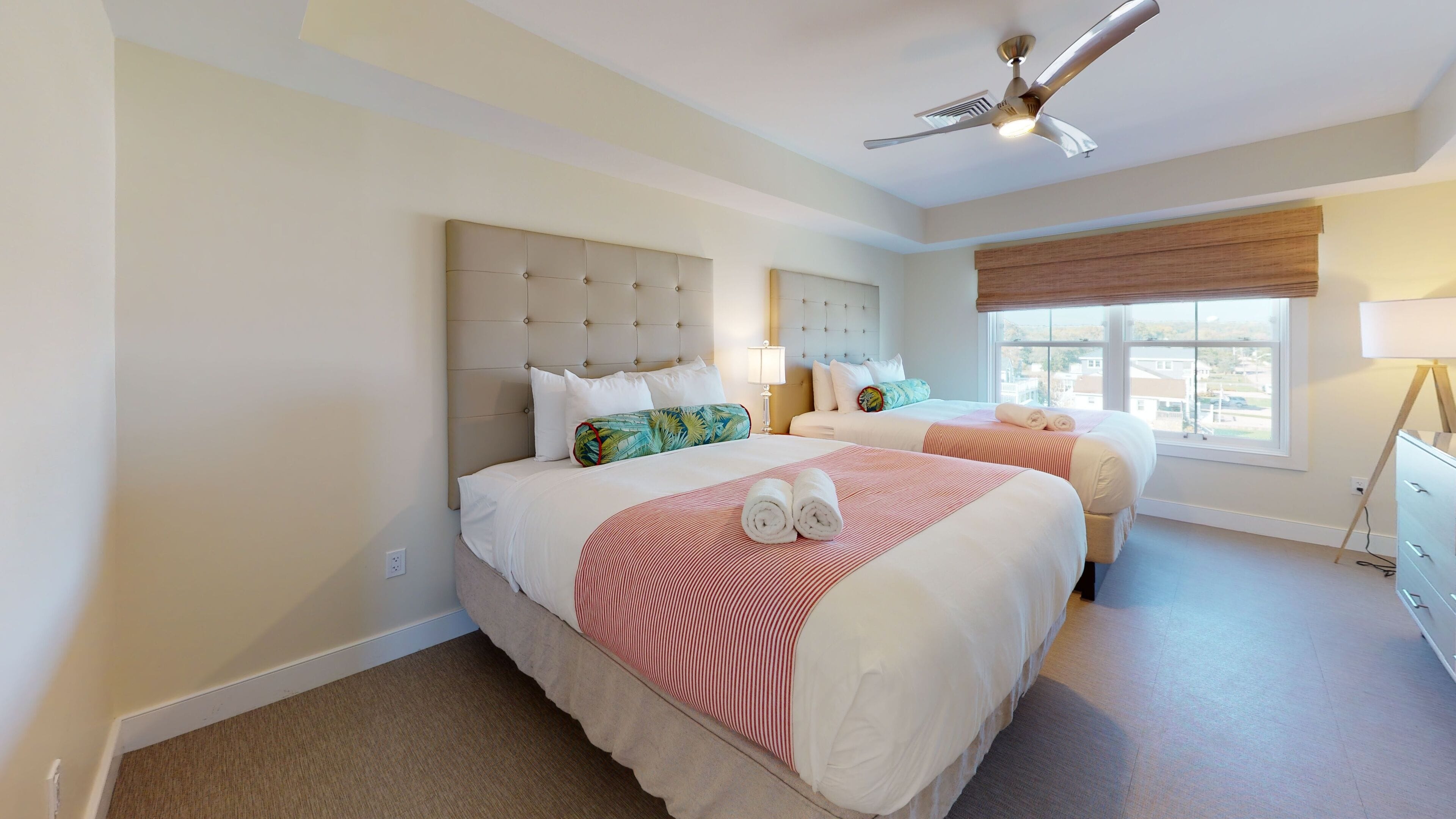 A hotel room with two beds, a ceiling fan, and a window with a view.