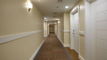 Un pasillo de hotel con pisos alfombrados, paredes blancas y puertas a ambos lados.