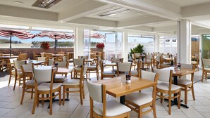 A spacious indoor dining area with wooden tables and chairs, large windows, and American flags. - The Hotel Maria (Westerly)