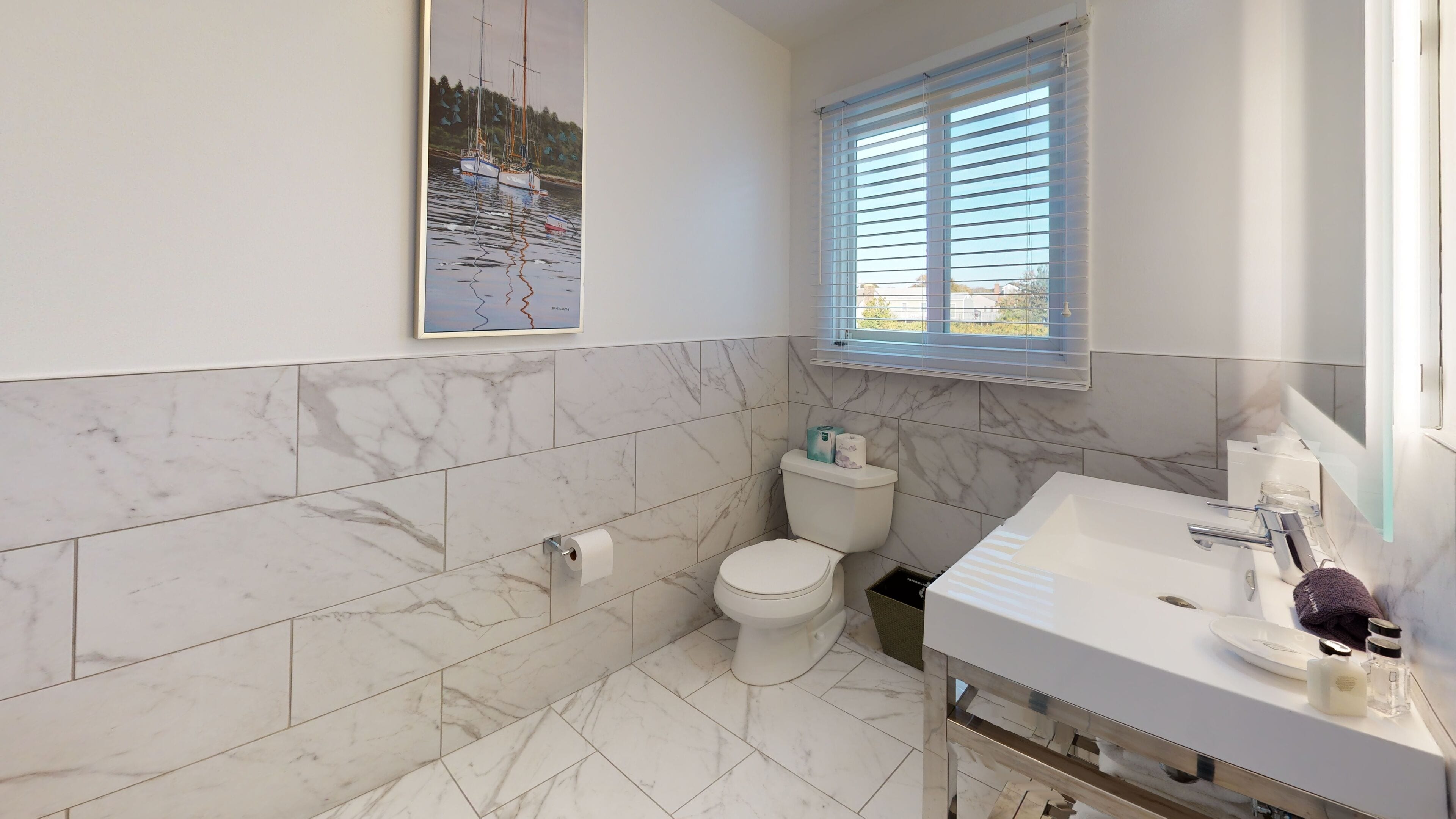 Une salle de bain avec des toilettes, un lavabo et une fenêtre équipée de stores.