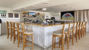 A bar area with a central island, bar stools, and a variety of bottles and glasses. - The Hotel Maria (Westerly)
