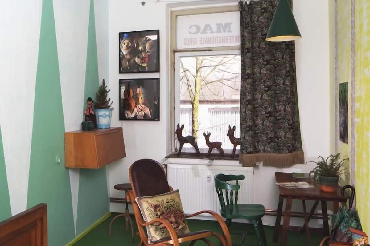 A cozy room with a bed, a rocking chair, a desk, and a window with a view of a building.