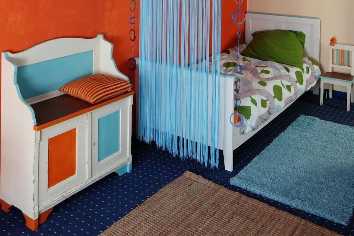 A bedroom with a bed, a chair, a mirror, and a painting on the wall.