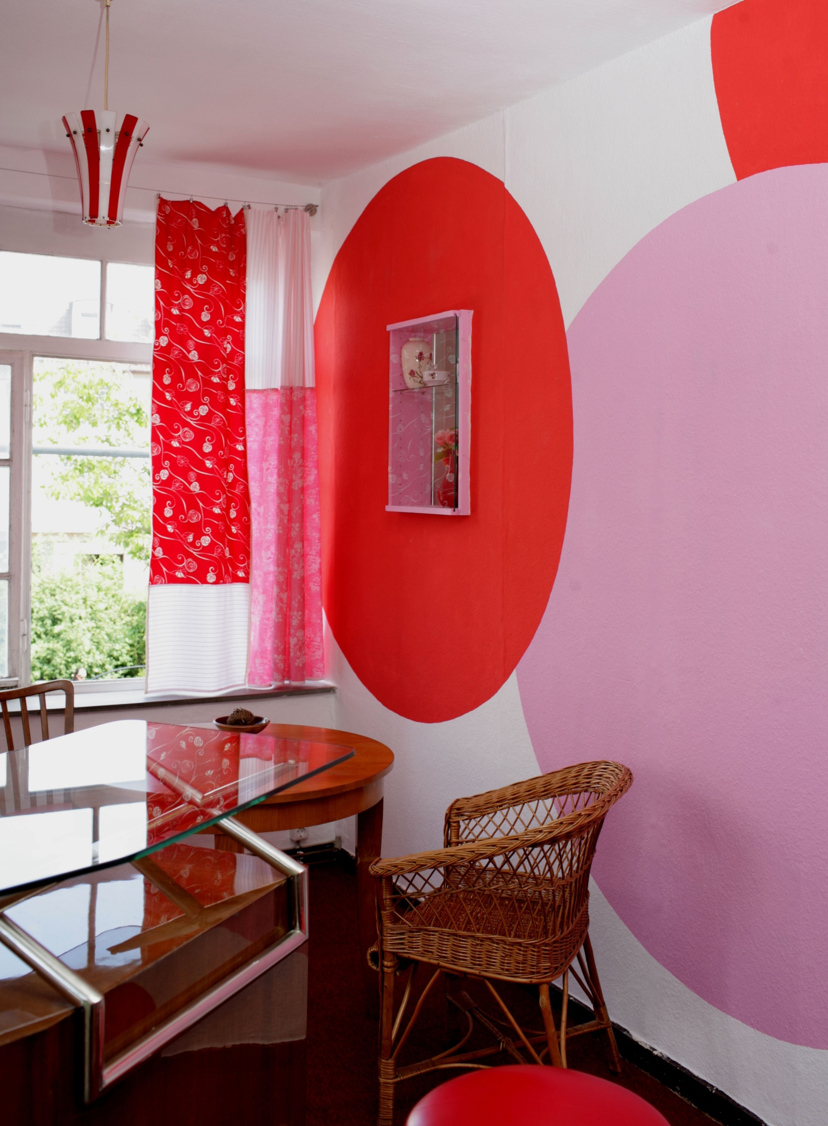 A dining area with a glass table, wicker chairs, and a red and white wall.