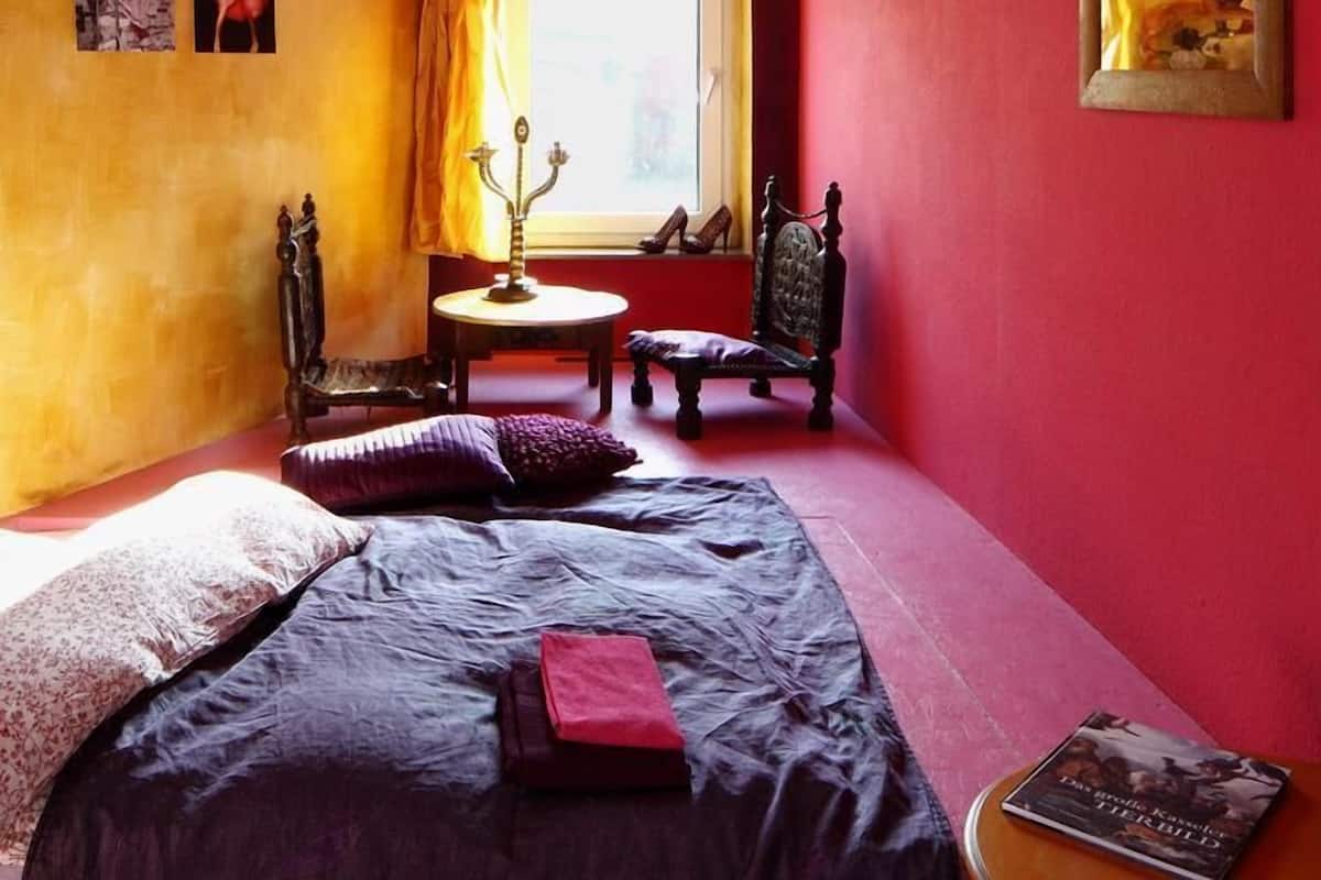 A room with a bed, a chair, a small table, and a window.