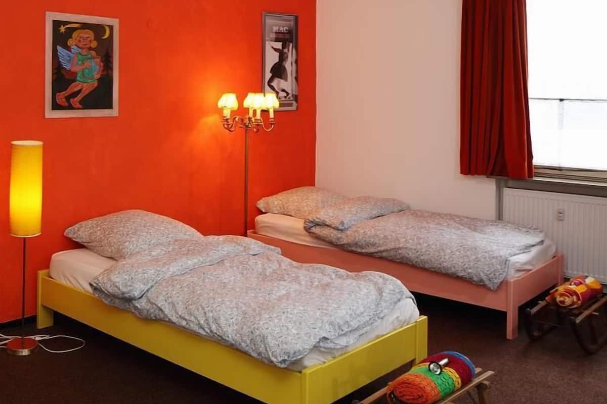 A room with two beds, a lamp, a rocking horse, and a window with red curtains.