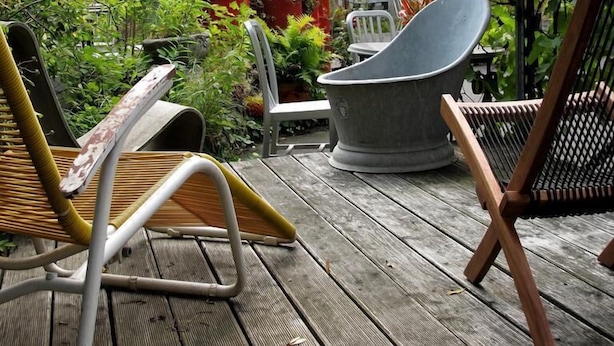 Una terraza de madera con dos sillas, una mesa y una planta en maceta.