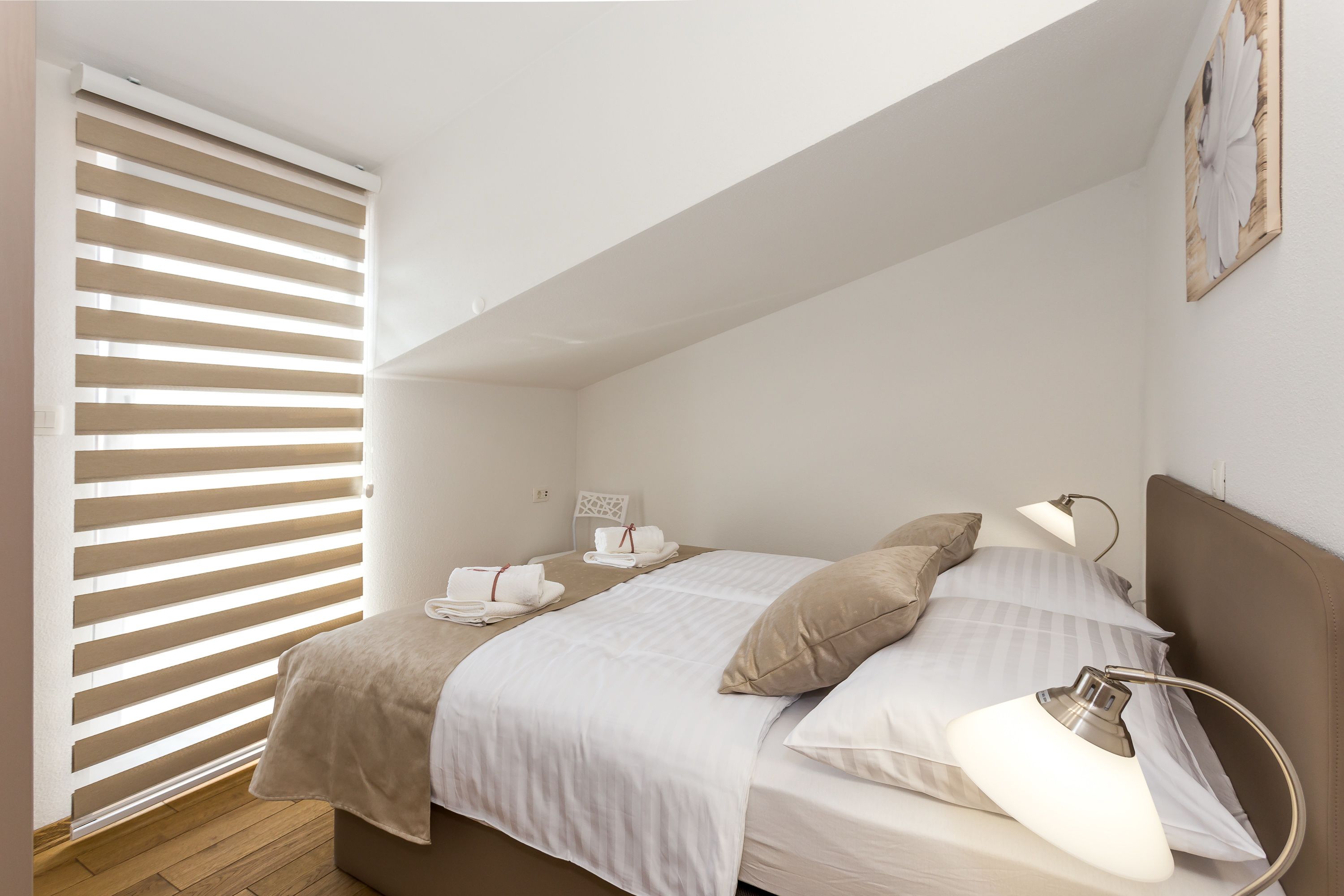 Een slaapkamer met een bed, nachtlampen en een raam met zonwering.