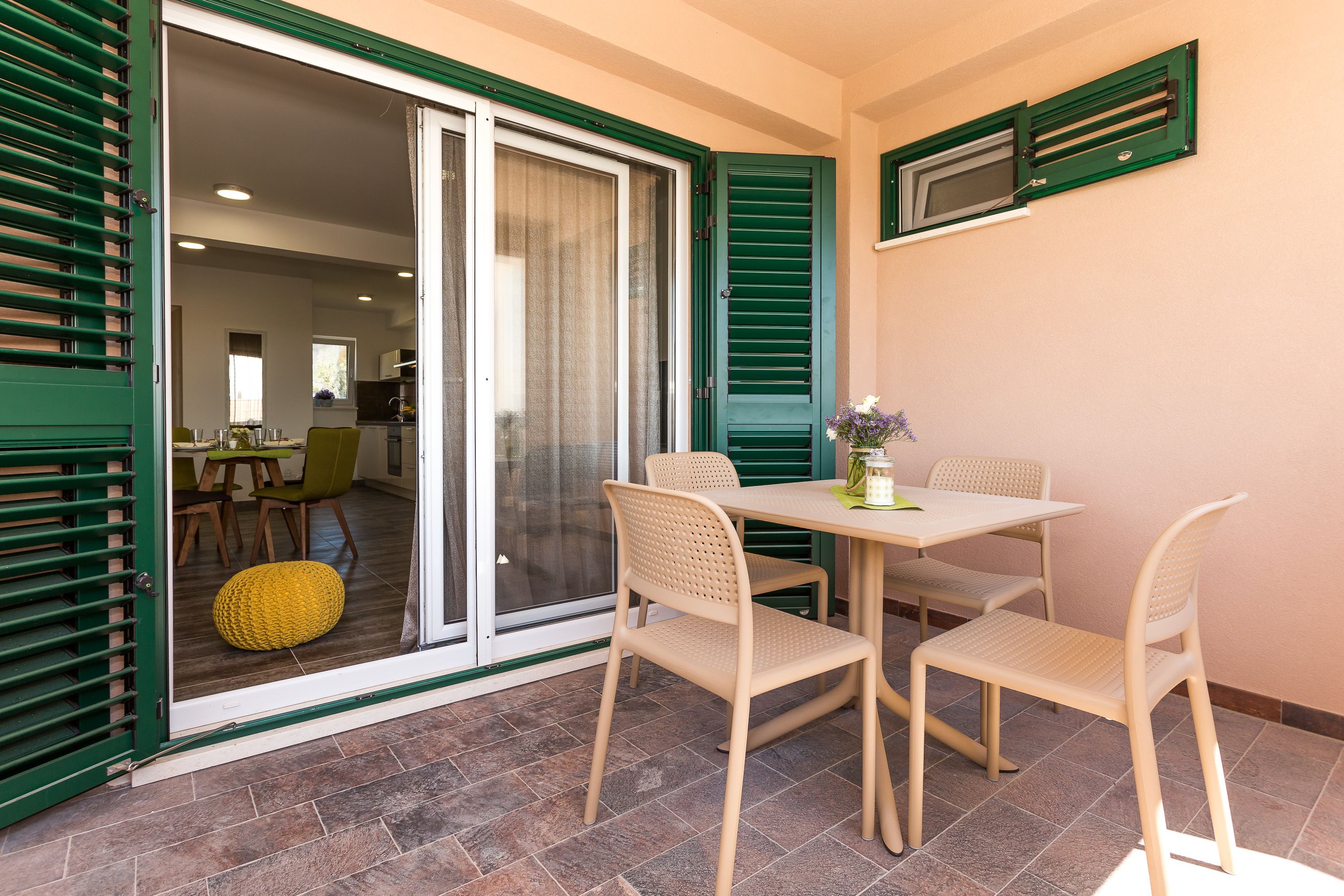 A dining area with a table and chairs, a sliding glass door, and a window with shutters.