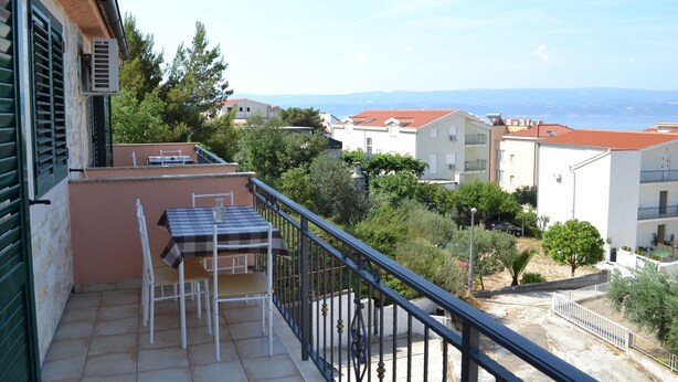 A balcony with a table and chairs, overlooking a residential area with houses and a distant view of the sea.