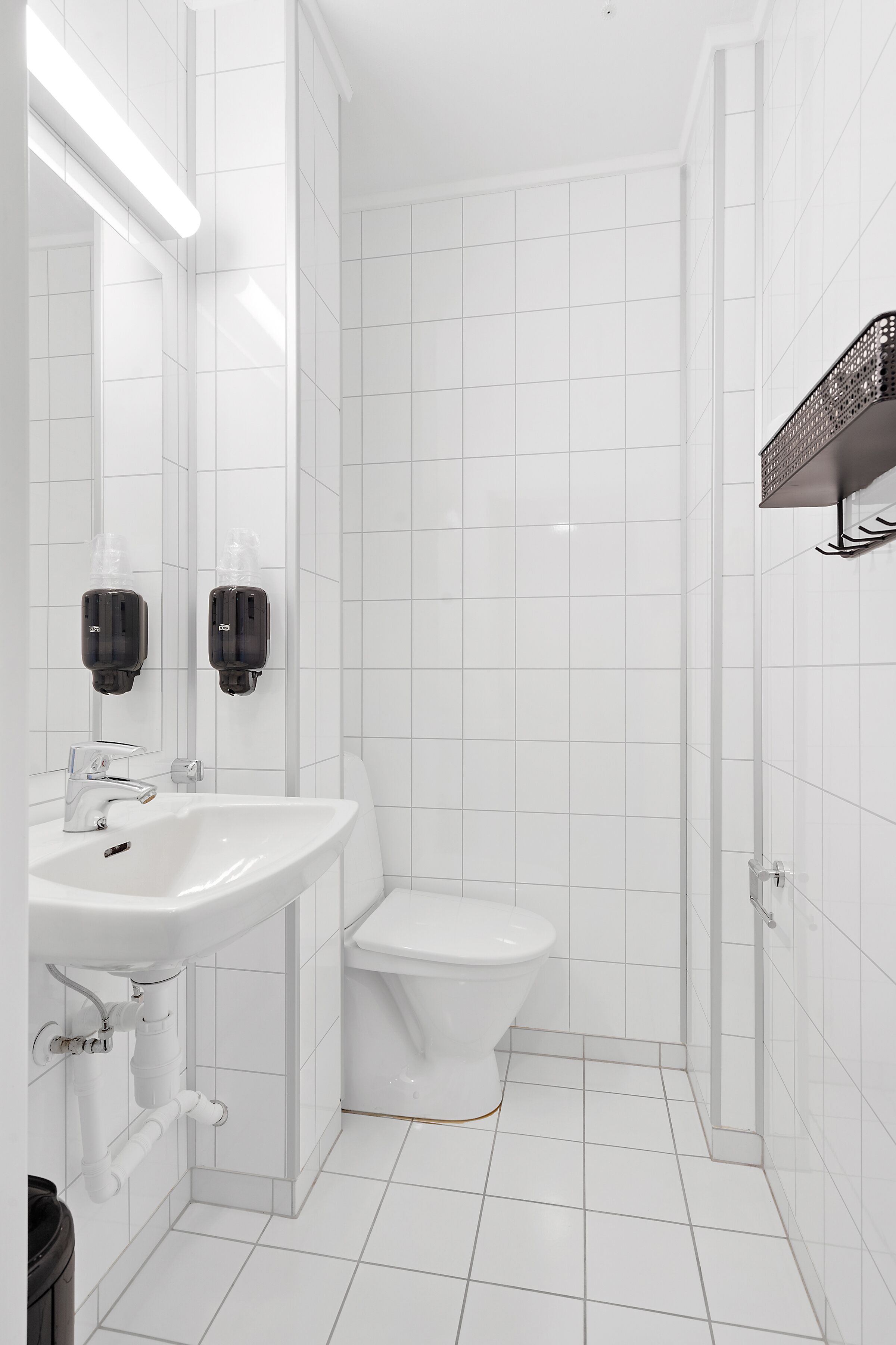 A modern bathroom with white tiles, a sink, a toilet, and a shower area.