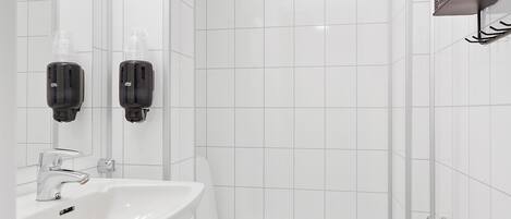 A modern bathroom with white tiles, a sink, a toilet, and a shower area.