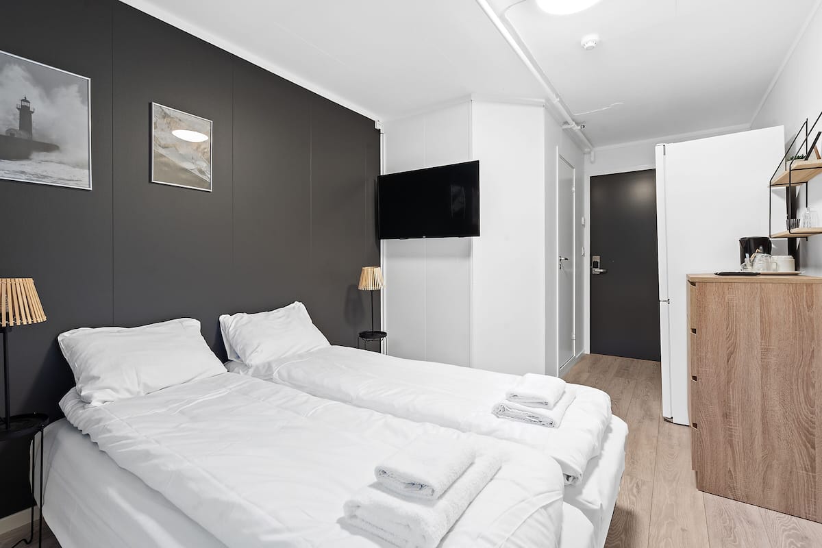 A modern hotel room with two beds, a flat-screen TV, a wooden cabinet, and artwork on the walls.