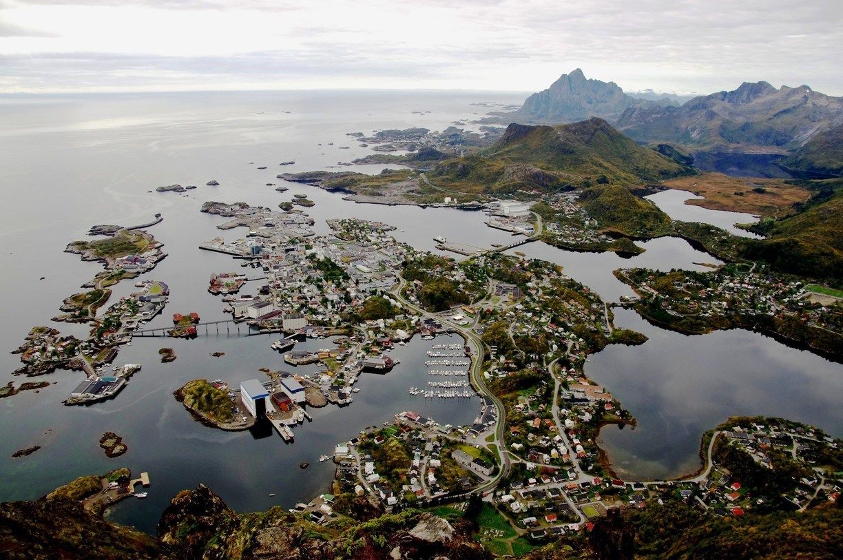 An aerial view of a coastal town with numerous docks and boats, surrounded by mountains and a large body of water.