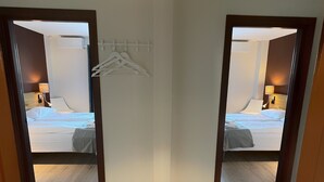 A hotel room with a wooden floor, a bed with white bedding, a hanging clothes rack, and a ceiling light fixture. - Marina Hotel Lofoten (Vagan)