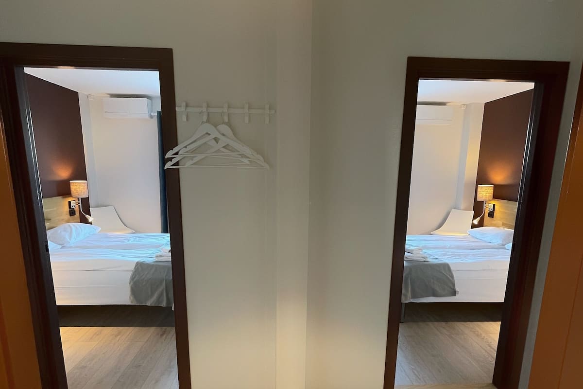 A hotel room with a wooden floor, a bed with white bedding, a hanging clothes rack, and a ceiling light fixture.