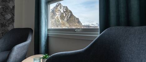 Een kamer met twee donkere fauteuils, een kleine ronde tafel met een kaars en een plant, en een raam met uitzicht op een berg.