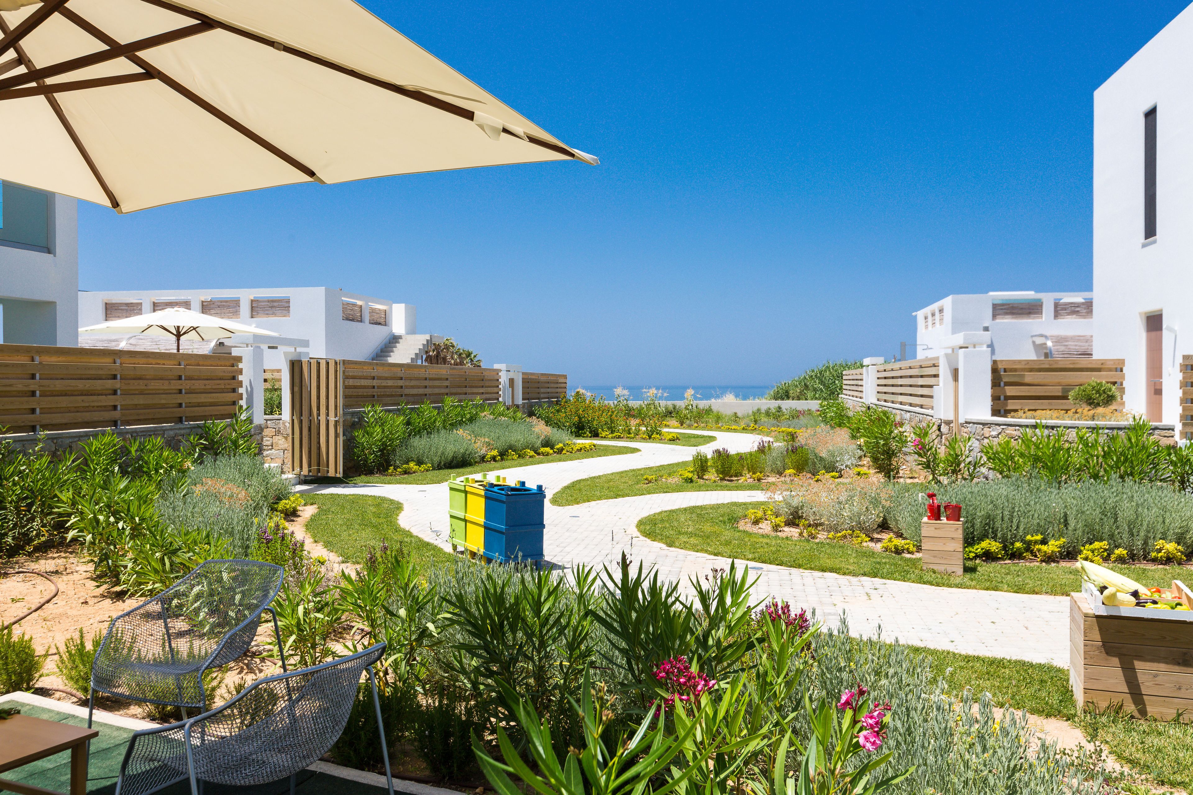 Un jardín ajardinado con un sendero sinuoso, mobiliario exterior y vistas al mar.