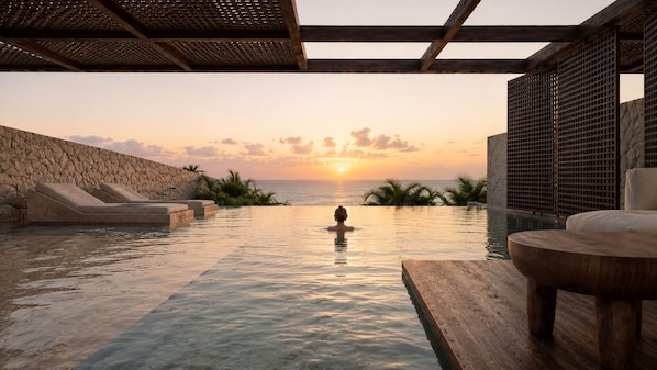 En infinitypool med utsikt över solnedgången, solstolar och ett trädäck.