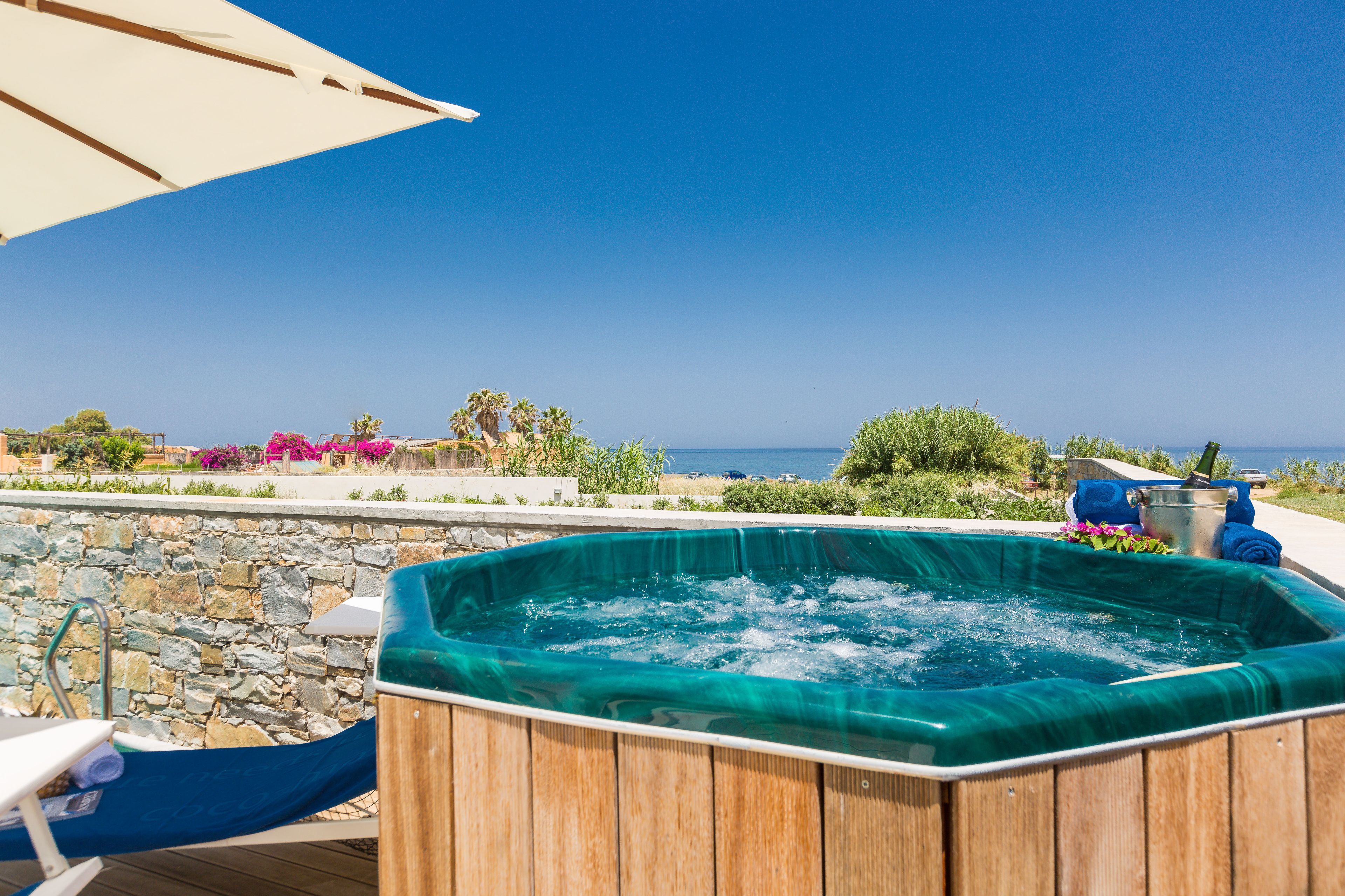 A wooden hot tub with a stone wall backdrop, a poolside chair, and a view of the ocean.