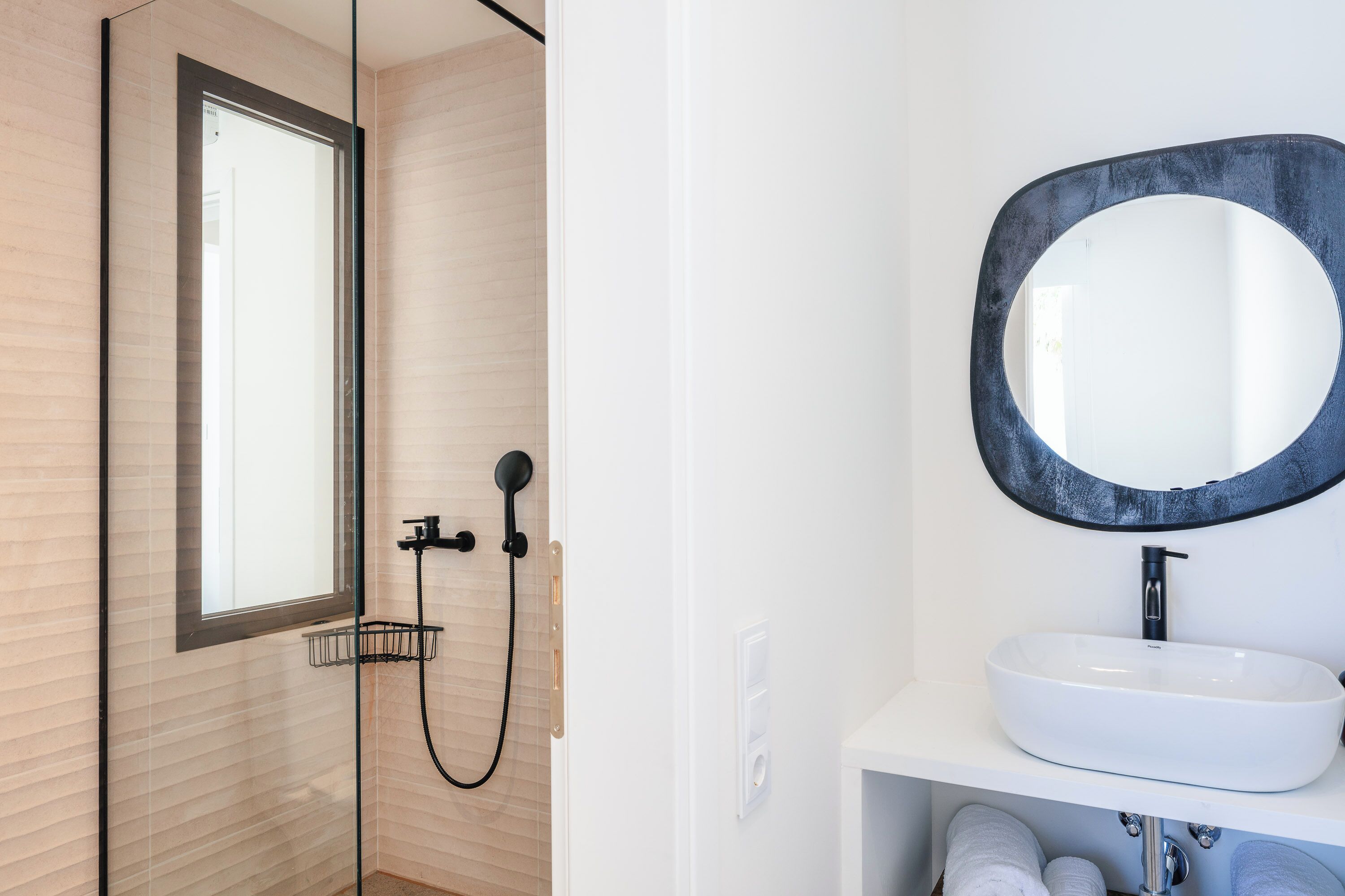 A modern bathroom with a glass shower enclosure, a white sink, and a large mirror.