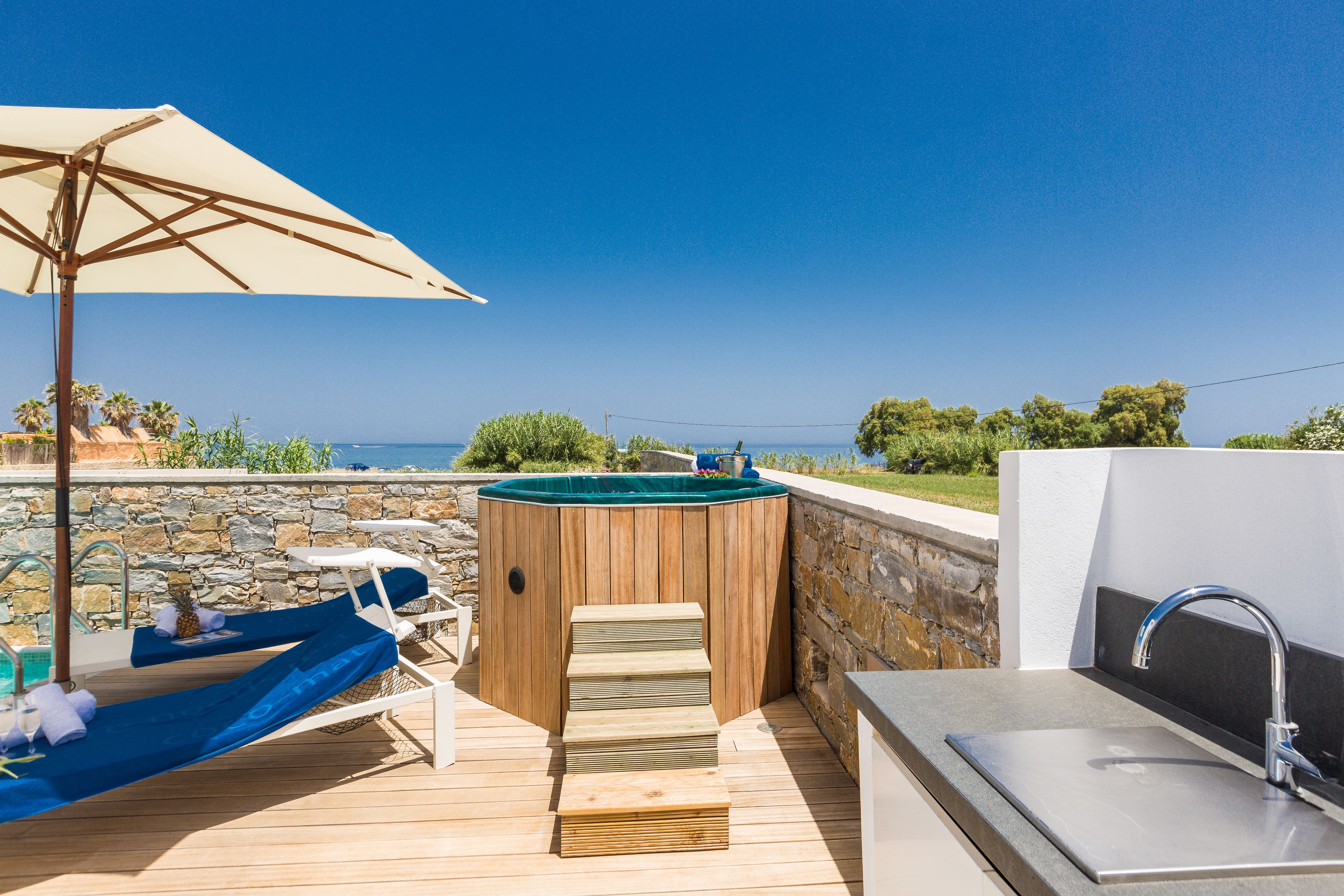Un patio in legno con idromassaggio, poltrone relax e un lavandino.