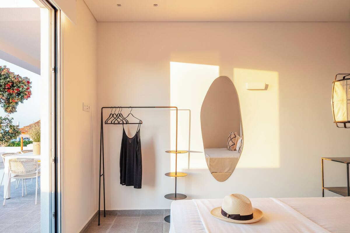 A modern hotel room with a bed, a hanging light fixture, a wall-mounted shelf, and a view of the outdoors.