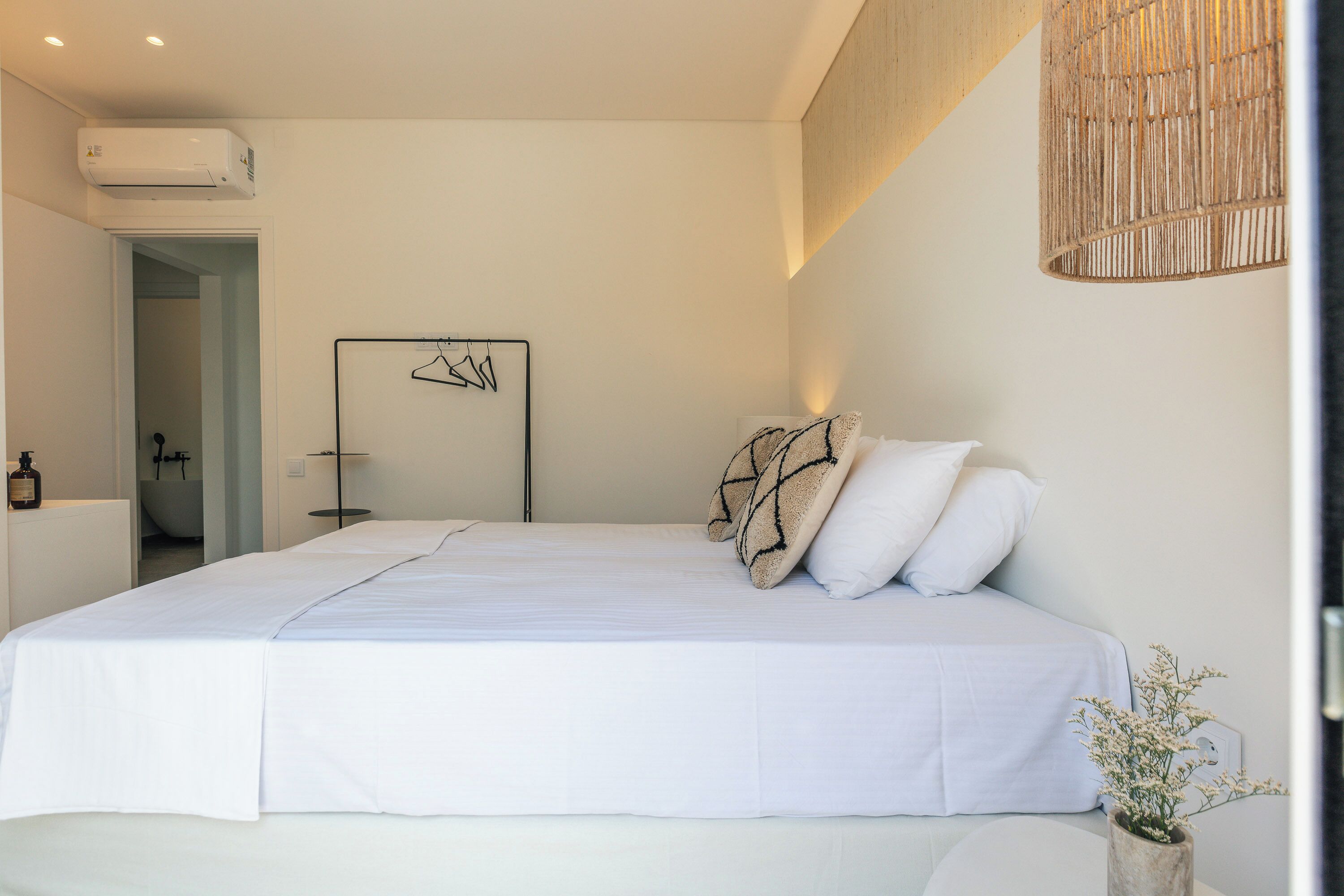 A modern bedroom with a large bed, a hanging light fixture, and a wall-mounted air conditioner.