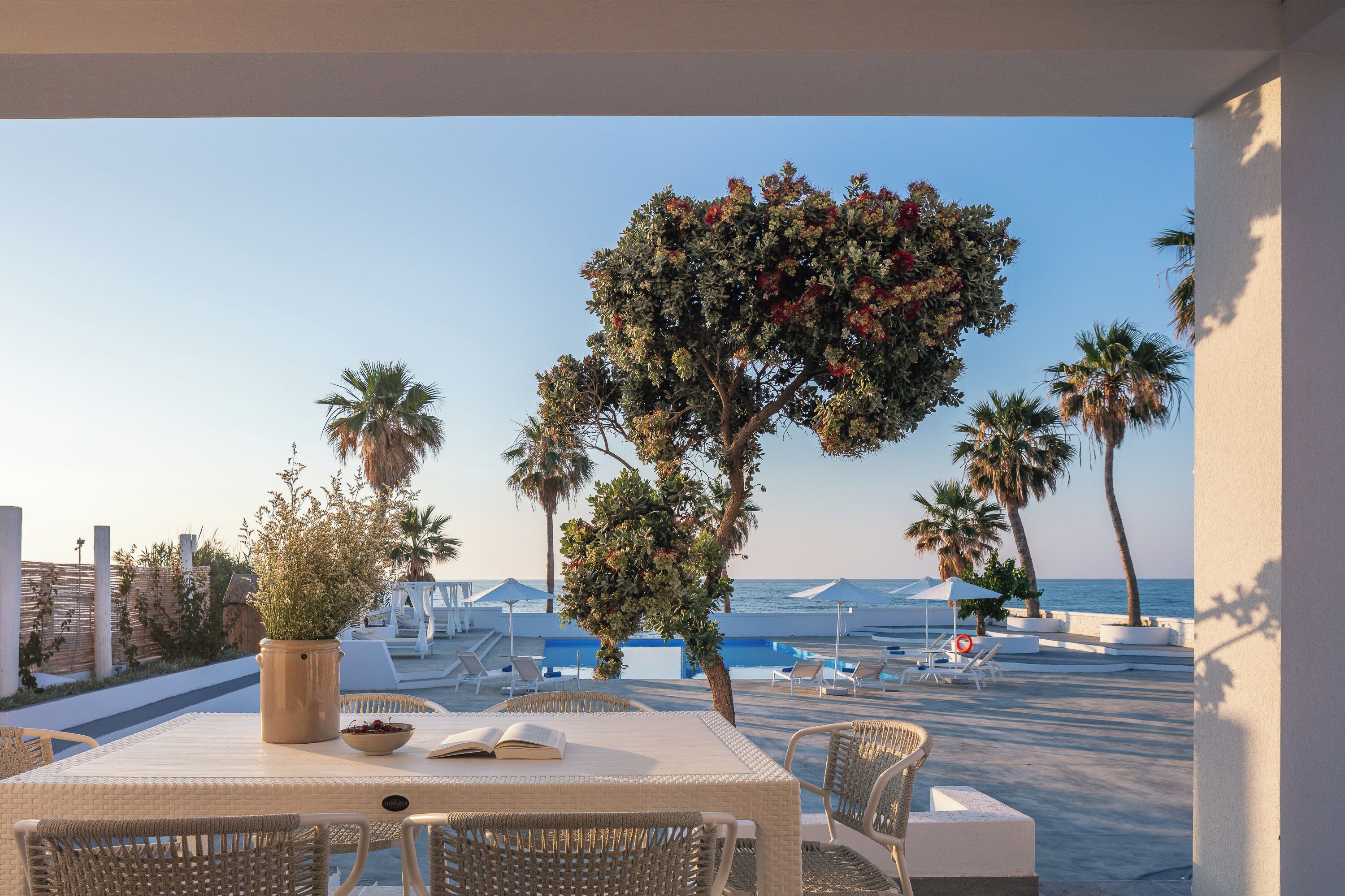 Une terrasse avec une table et des chaises, donnant sur une piscine et la mer.