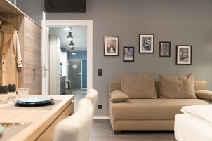 A modern living room with a beige sofa, a wooden dining table, and framed pictures on the wall.