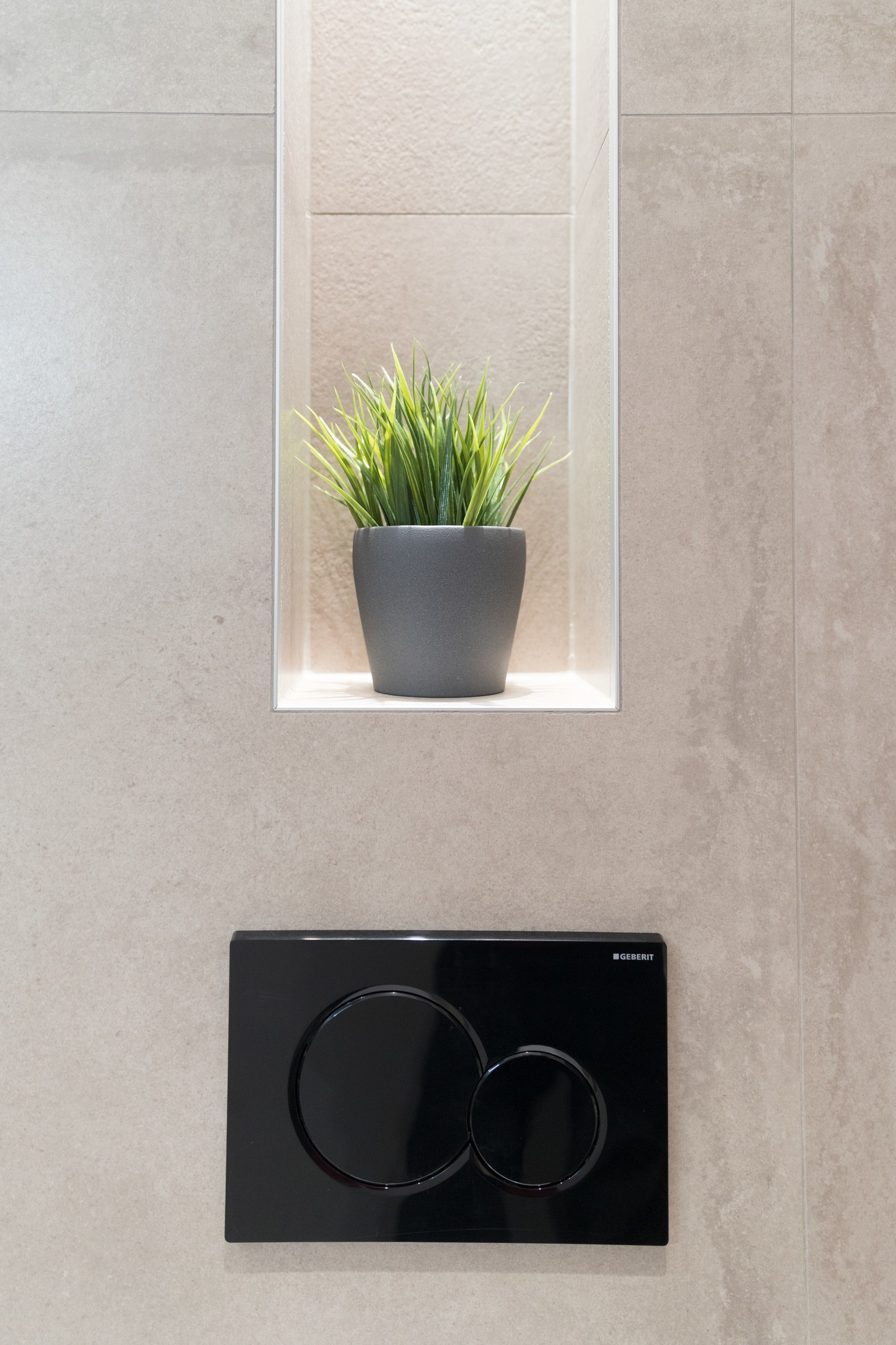 Un baño moderno con una planta en maceta en una ventana, un panel de control negro y una pared con textura.