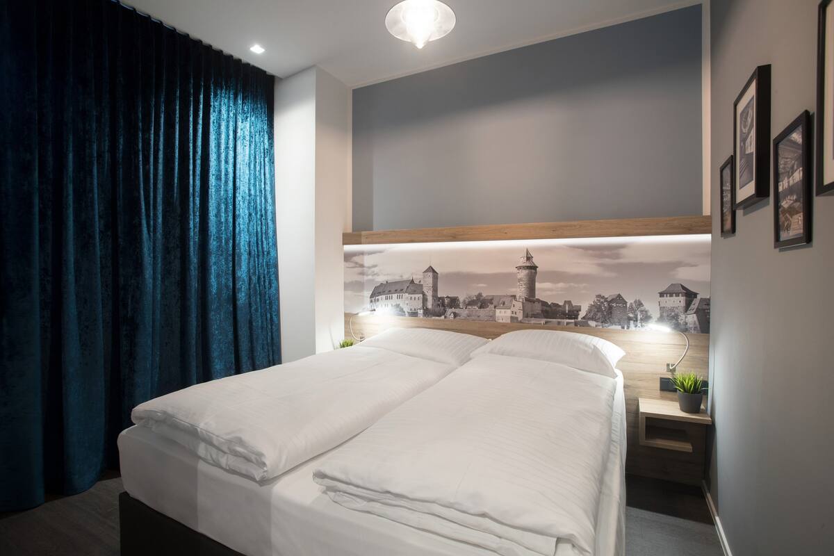 A modern hotel room with a large bed, a nightstand with a lamp, and a cityscape mural on the wall.