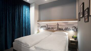Una habitación de hotel moderna con una cama grande, una mesita de noche con lámpara y un mural con vista a la ciudad.