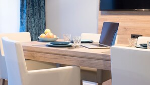 A modern dining area with a wooden table, white chairs, a laptop, and a bowl of fruit. - Aparthotel by dasPaul (Nuremberg)