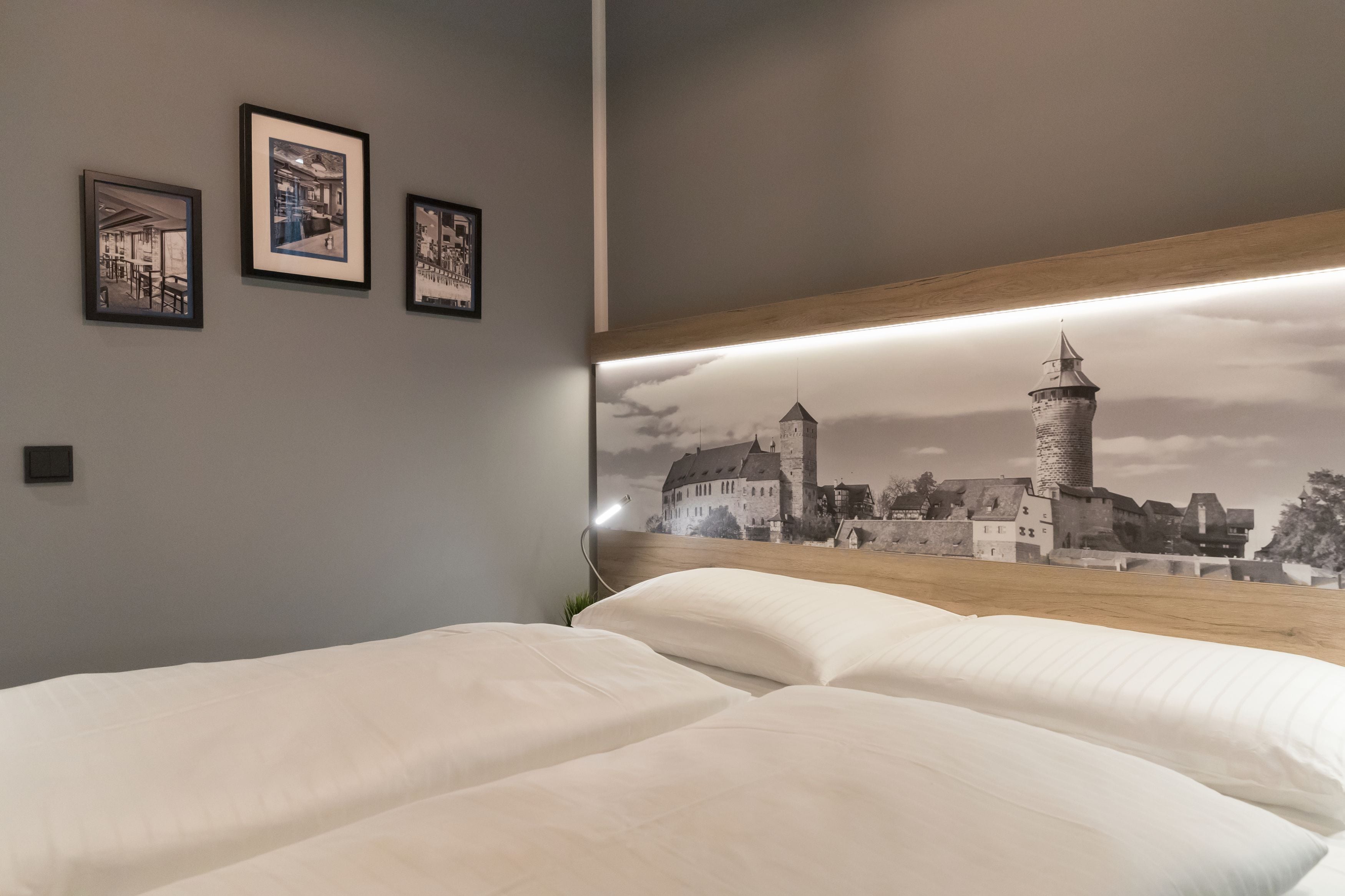 Une chambre à coucher avec un grand lit, une tête de lit ornée d’une fresque représentant un paysage urbain, et trois tableaux encadrés accrochés au mur.