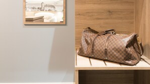 A room with a wooden wall, a hanging light fixture, a mirror with a view of a building, and a bench with a bag. - Aparthotel by dasPaul (Nuremberg)