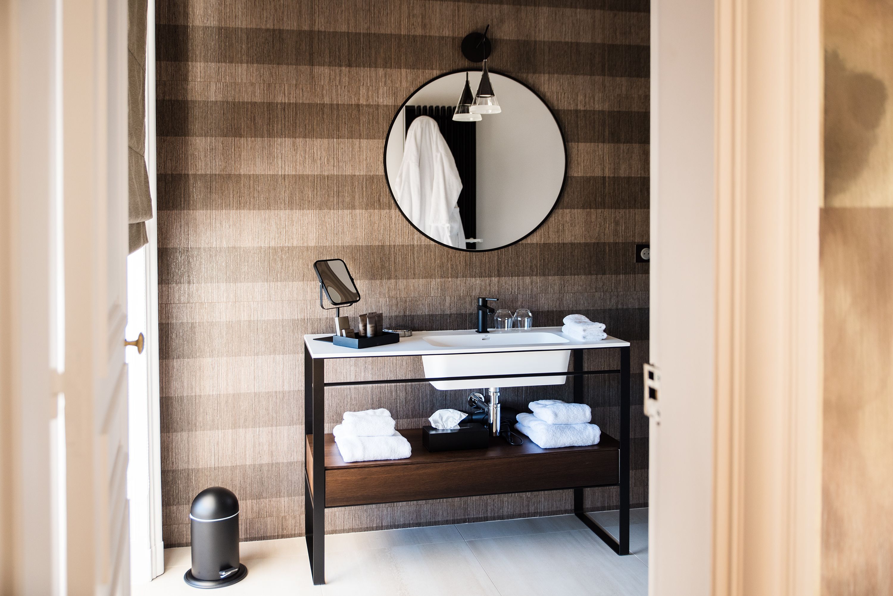 Un bagno moderno con uno specchio rotondo, un lavandino bianco e un mobile contenitore in legno.