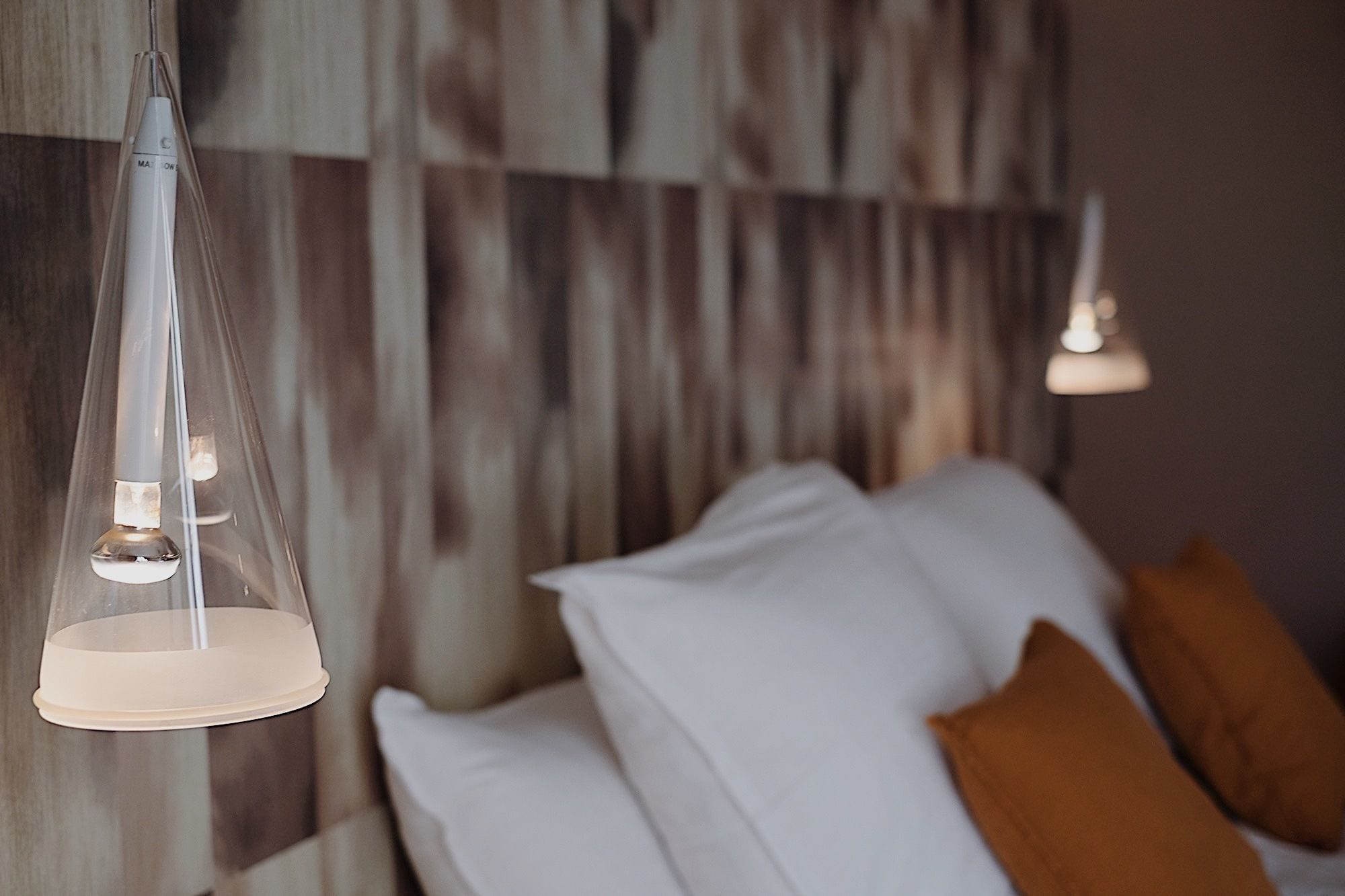A modern bedroom with a wooden headboard, a bed with white and brown pillows, and two pendant lights.