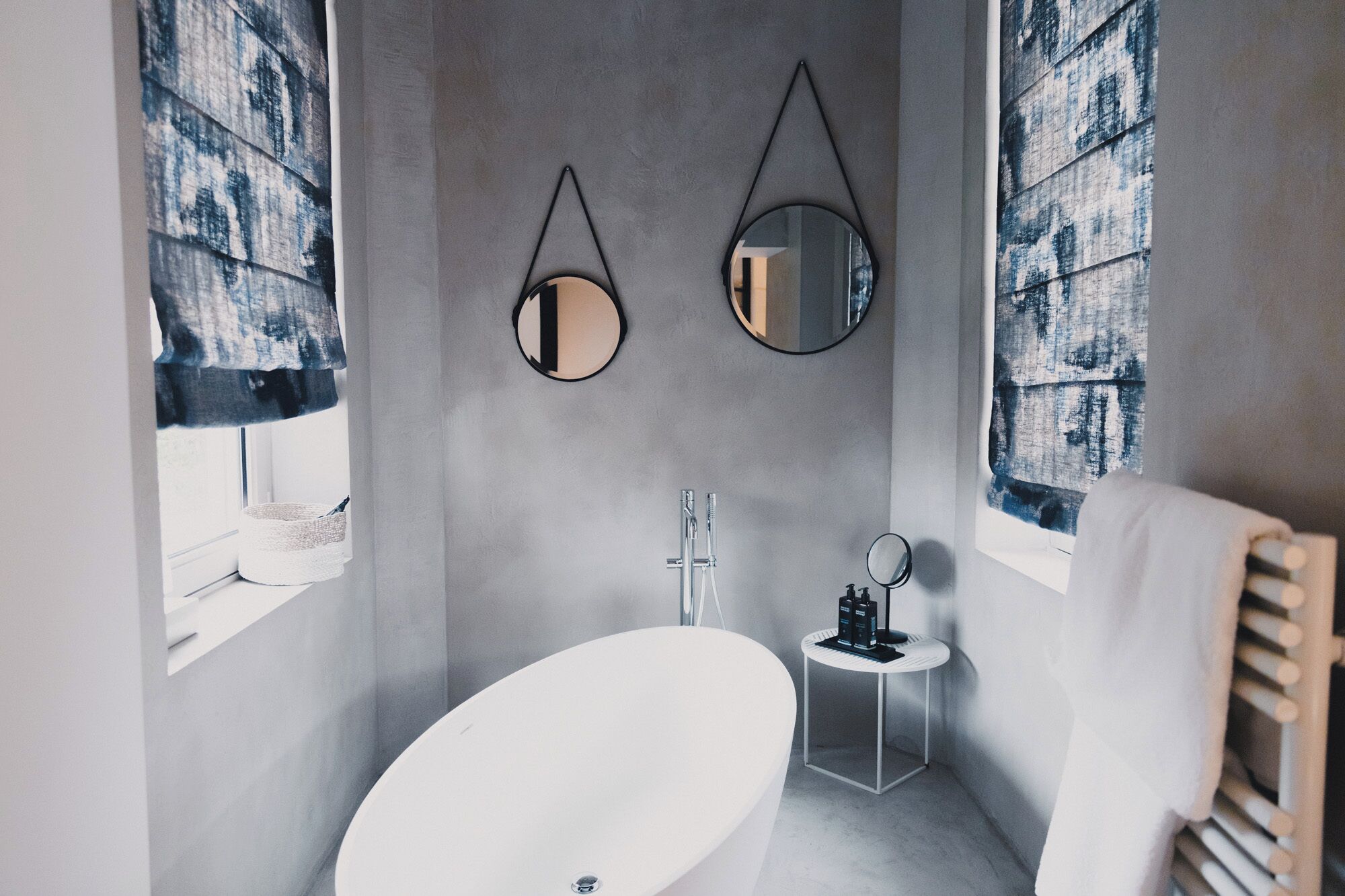 Ein modernes Badezimmer mit einer freistehenden Badewanne, zwei Wandspiegeln und einem kleinen Schminktisch mit Pflegeprodukten.
