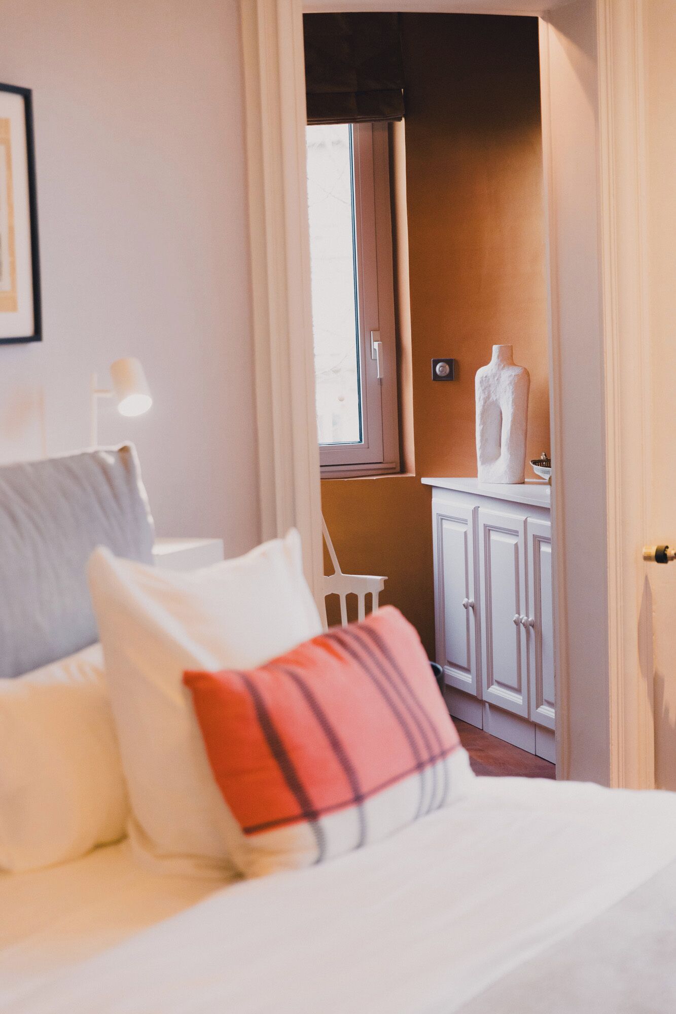 Un dormitorio con cama, almohadas, una mesita de noche, una lámpara y vistas a un baño con inodoro y espejo.