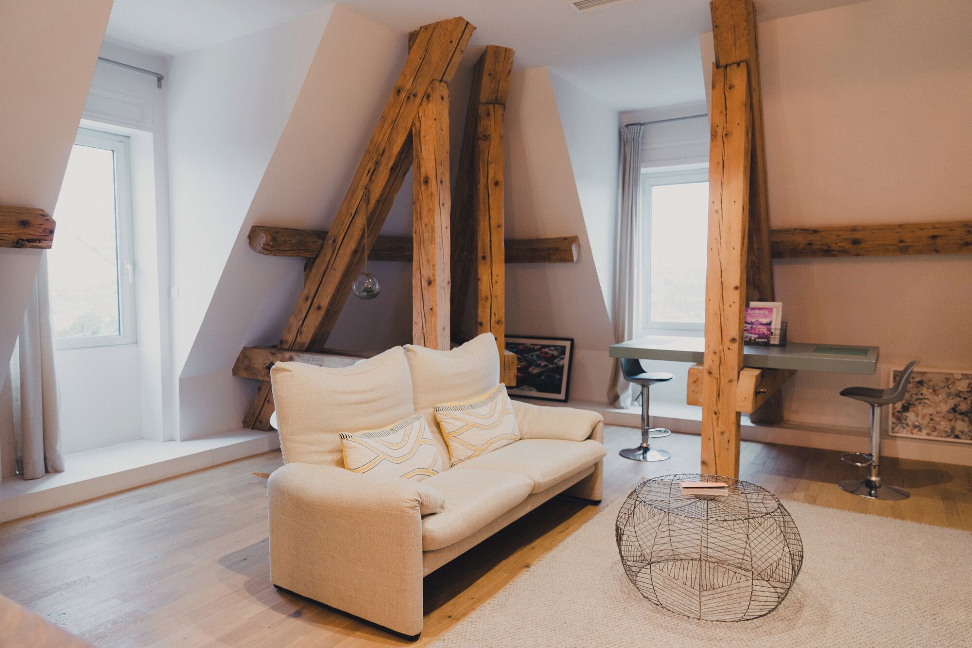 A cozy loft bedroom with a sofa, a round wire coffee table, and exposed wooden beams.