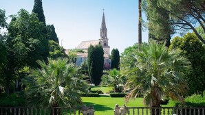 A church with a tall spire, surrounded by lush greenery and palm trees. - La Villa Guy & Spa - Teritoria (Béziers)