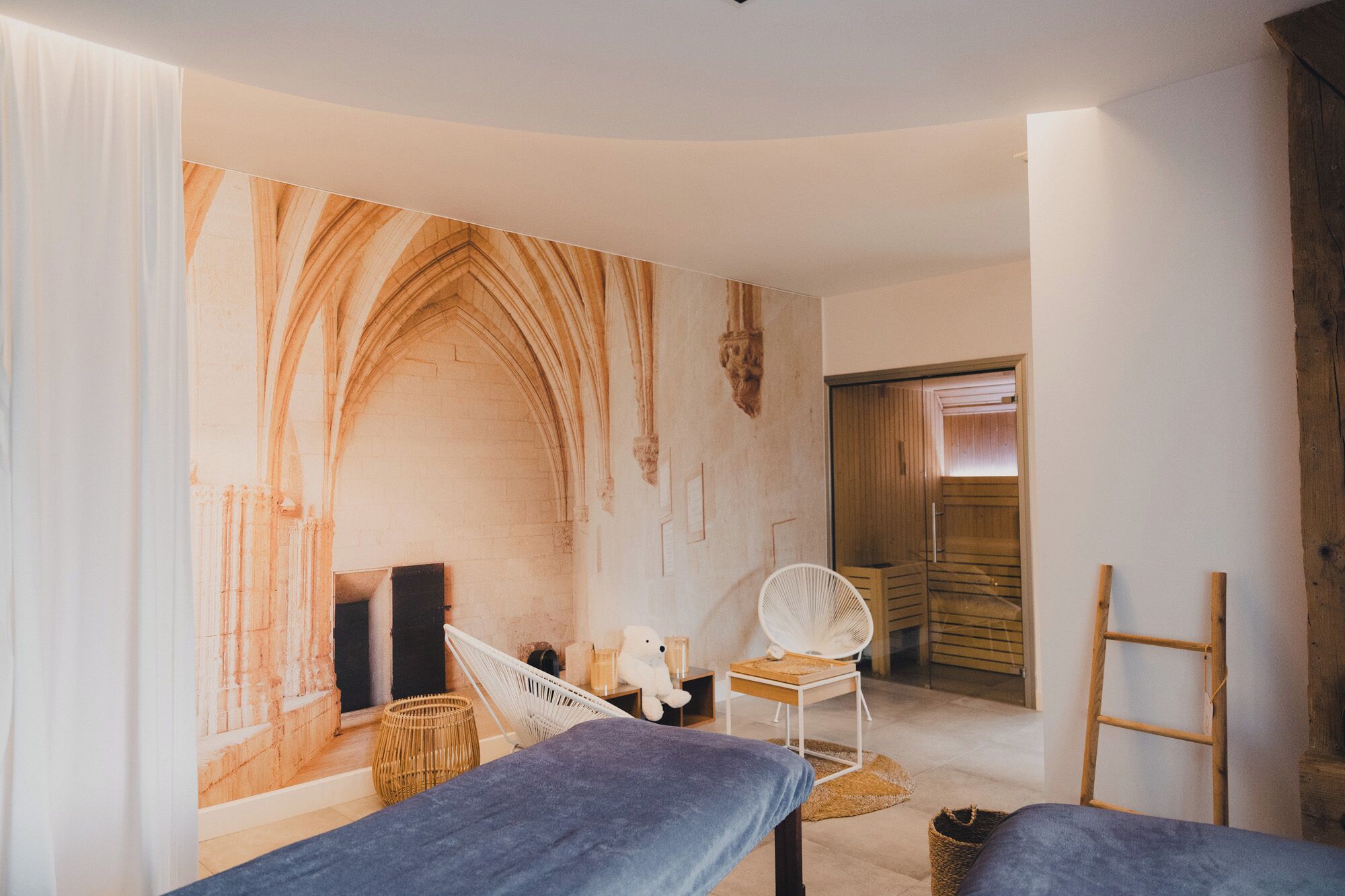 A room with a large arched wall, a white chair, a small table, and a wooden ladder.