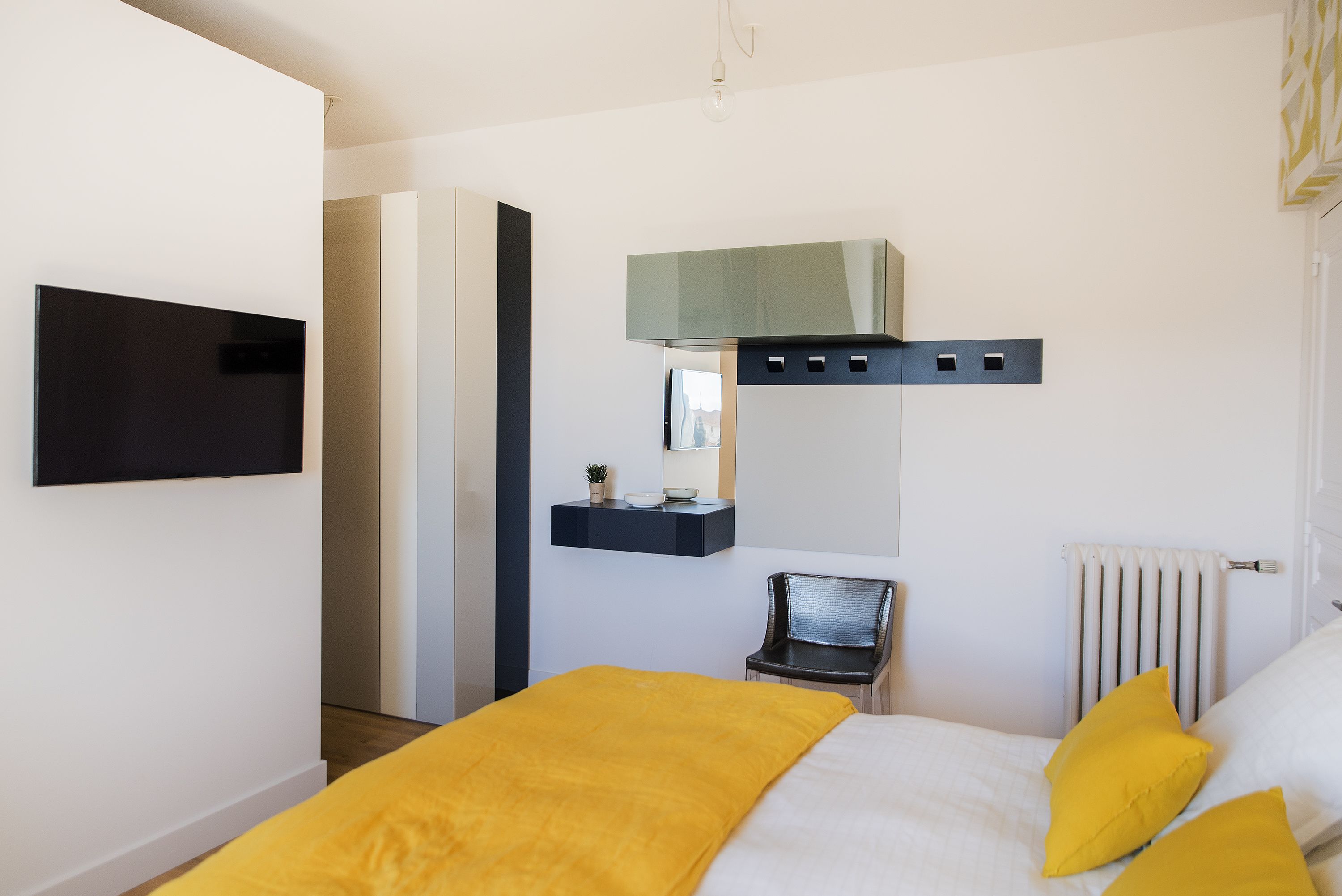 A modern hotel room with a bed, a flat-screen TV, a small seating area, and a window with blinds.