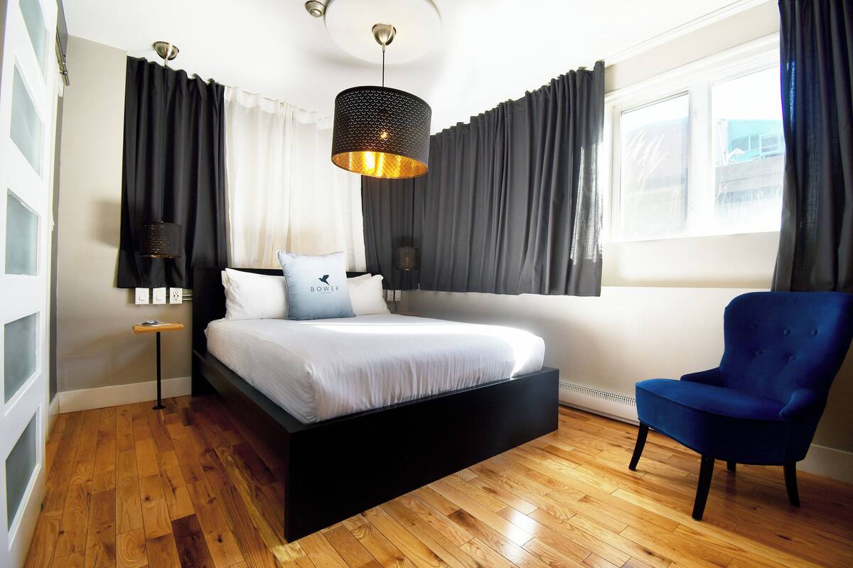 A bedroom with a bed, a chair, a bedside table, a lamp, and a window.