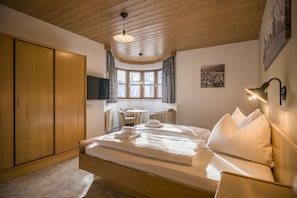 A bedroom with a large bed, wooden wardrobe, a small table, and a window with curtains. - Gasthaus Kammerhof (Angath)