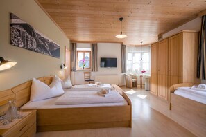 A hotel room with two beds, a TV, wooden furniture, and a painting on the wall. - Gasthaus Kammerhof (Angath)