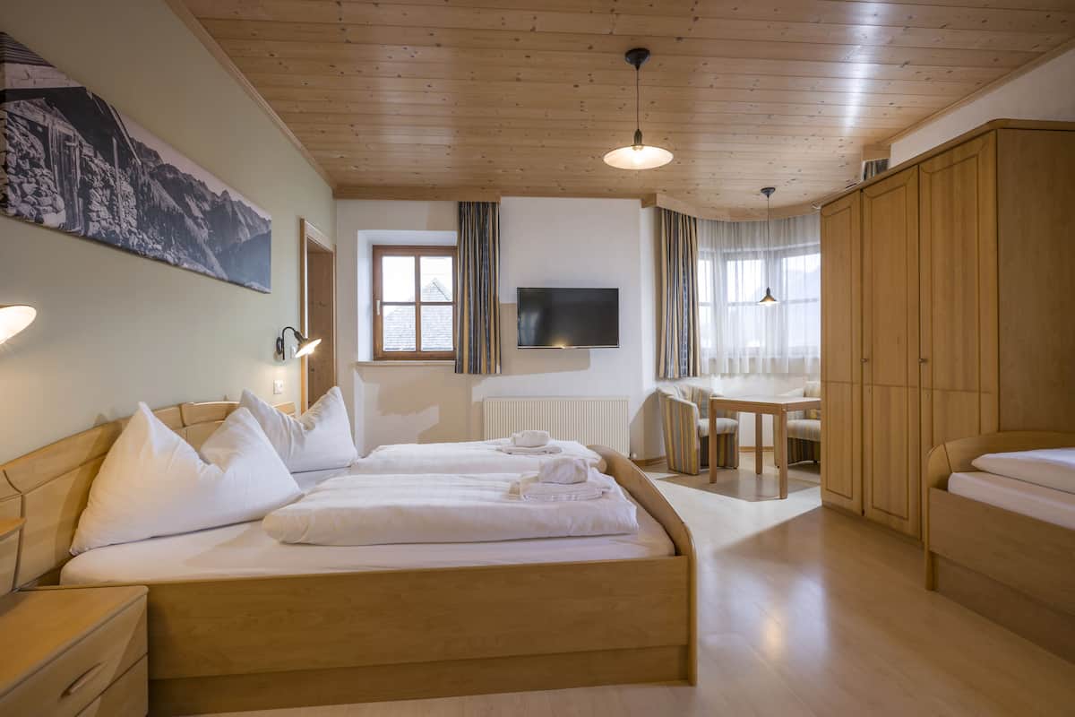 A hotel room with a wooden bed, a desk, a chair, a TV, and a wardrobe.