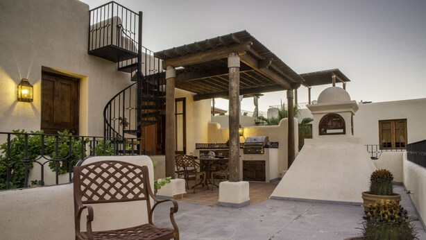 A patio with a wooden chair, a table, a grill, and potted cacti.