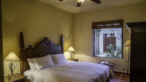 A bedroom with a wooden bed, two bedside tables with lamps, a ceiling fan, and a window with a view of the outside.